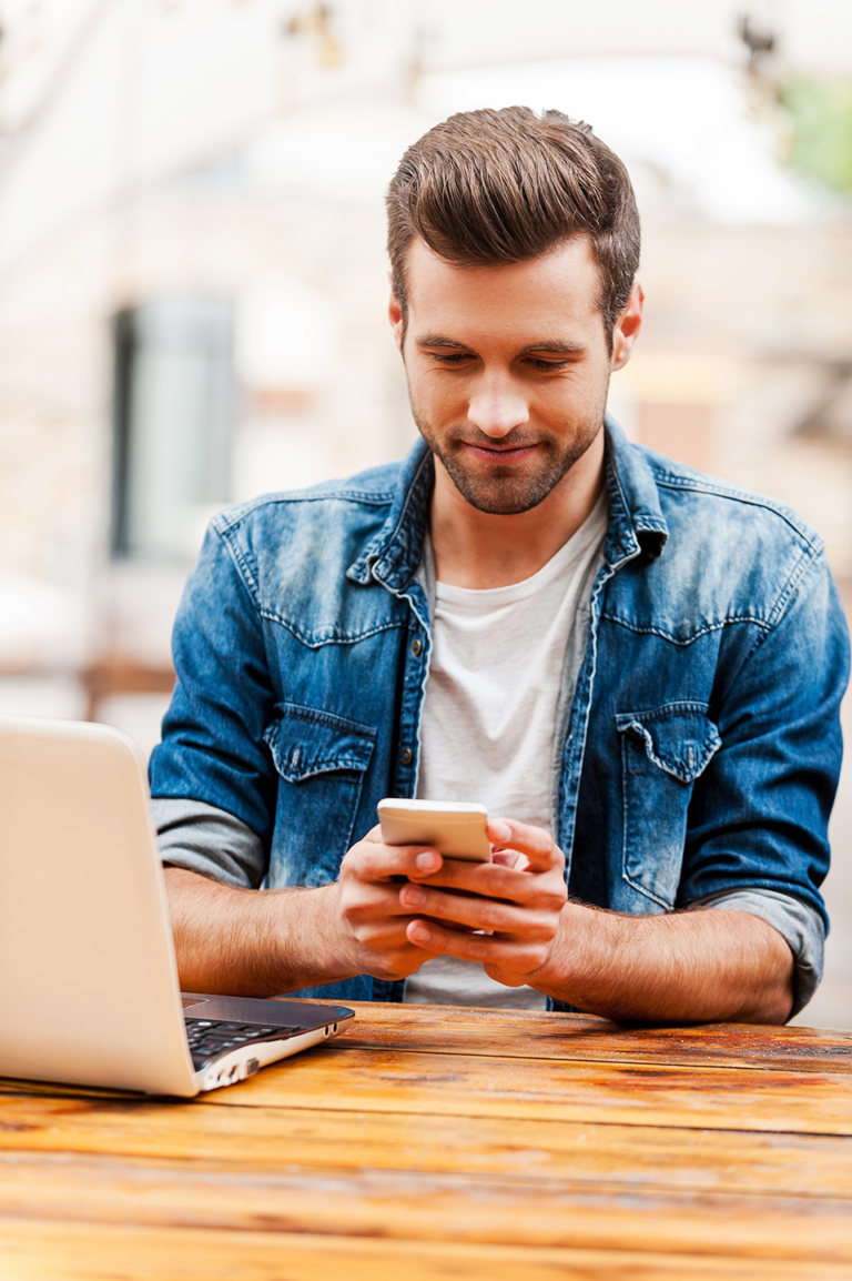 Young man checking his credit report from his mobile device while sitting at a table outside.